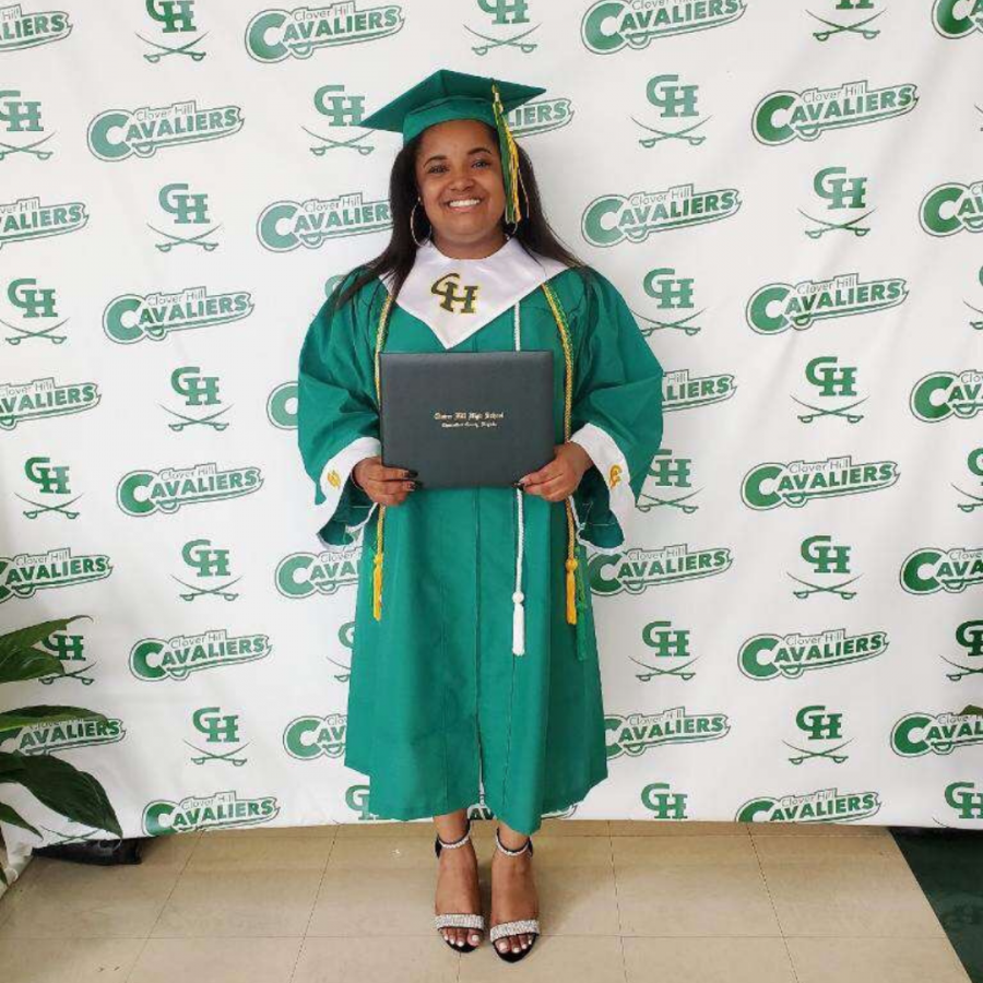 Deane stands with her diploma in front of a Clover Hill backdrop.