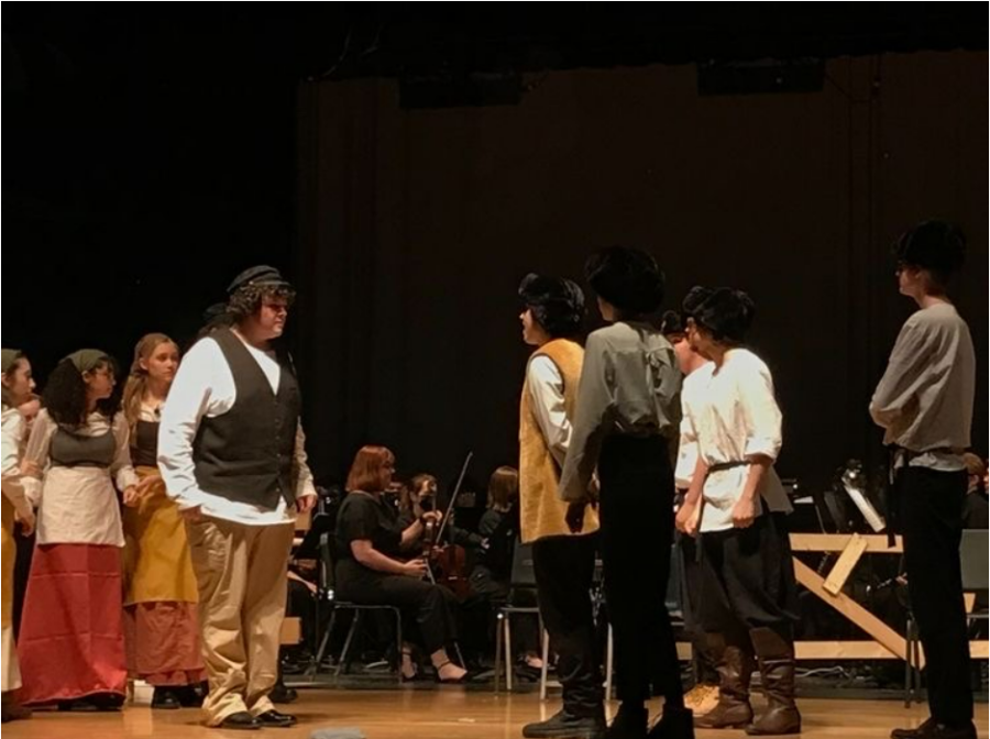 The cast of Fiddler on the Roof performs while the pit orchestra plays in the background. 