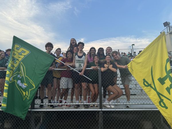 Students in the student section posing for a picture while showing their Cavalier pride in between two flags.