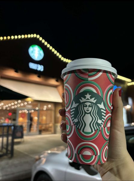 Starbucks holiday cup being held out in front of a Starbucks location.