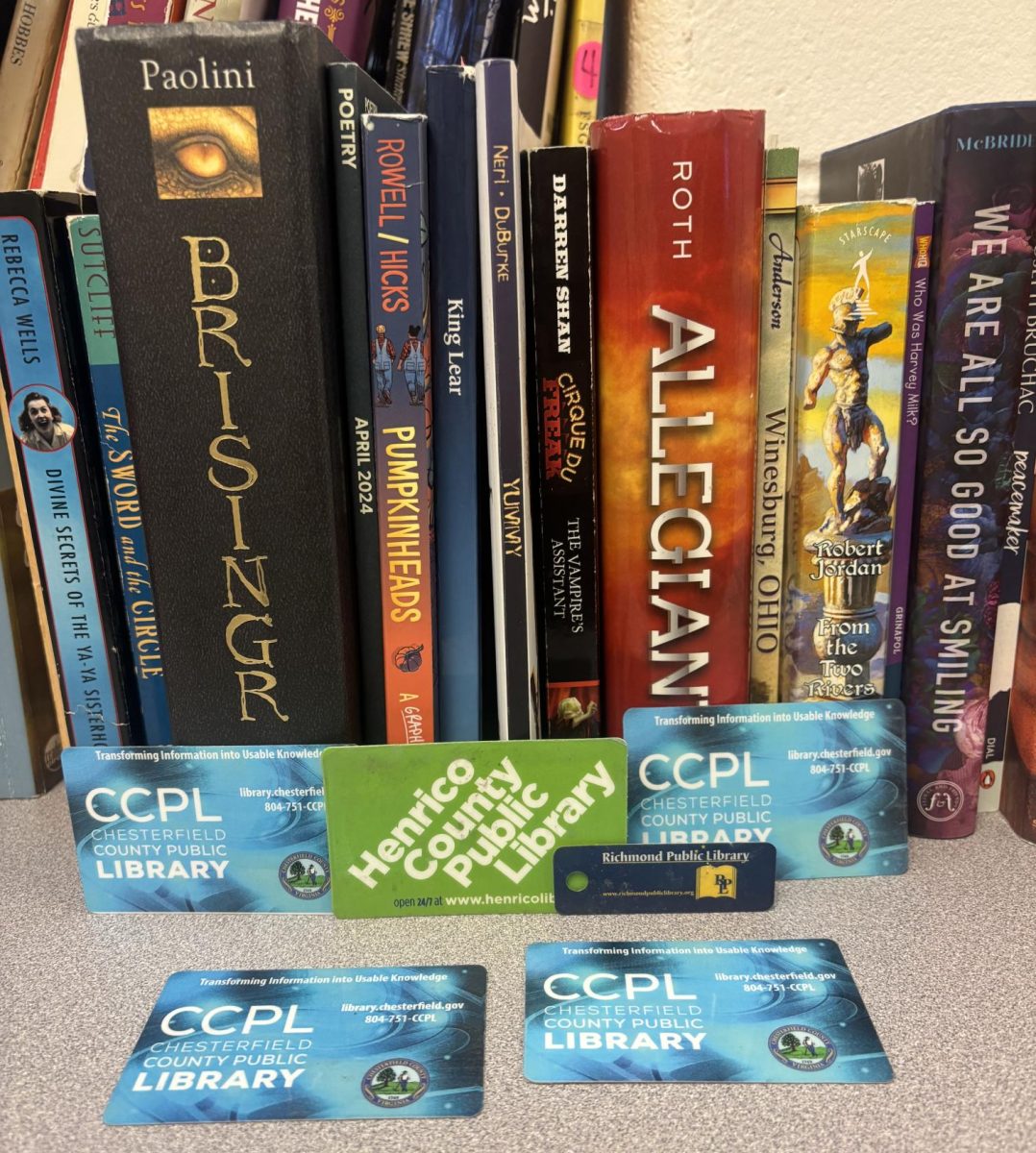 Four Chesterfield County Public Library cards, one Henrico County Public Library card, and one Richmond Public Library keychain card set up in front of a row of books.