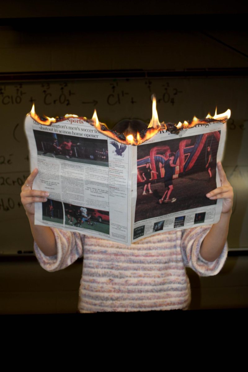Student holding a newspaper set on fire held out to cover their face.