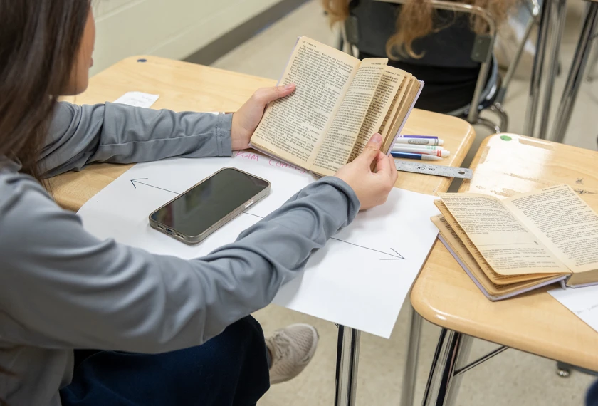 Student holding up a book in front of their phone it hide it